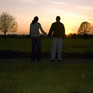 A couple standing hand-in-hand in front of a sunset.