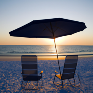 A beach at sunset with an umbrella and two beach chairs.