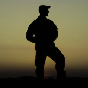 A silhouette of a soldier in military fatigues standing in a prepared stance against a sunrise.