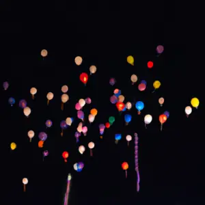 A group of balloons in a variety of colors floating up into the night sky.